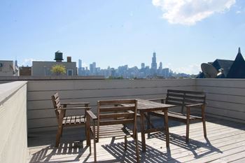 A wooden table and chairs are on a balcony with a city skyline in the background.